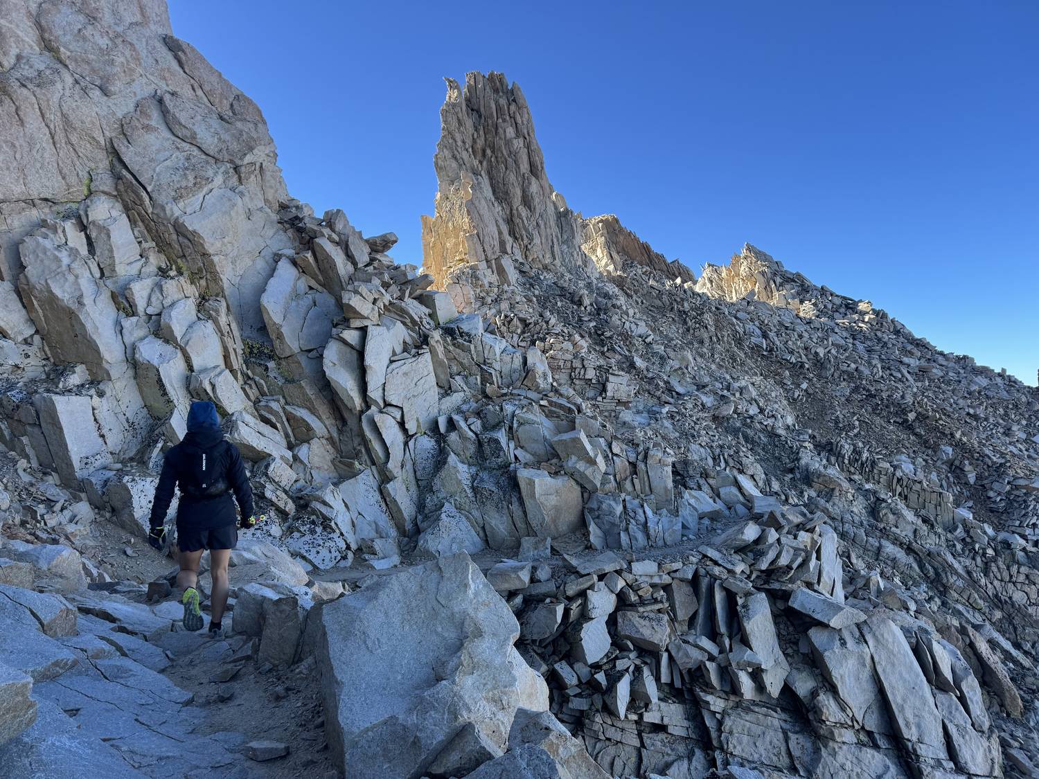 Hiker crossing granite talus below a rock spire on the Mount Whitney Trail